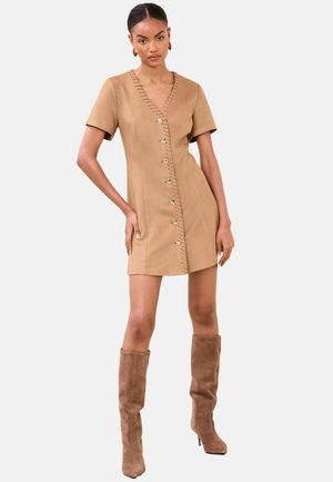 Īsām piedurknēm, bēša zamša kleita ar dziļu V-veida kakla izgriezumu un dekoratīvām pogām priekšpusē; kombinēta ar ceļgalu augstiem bēša zamša zābakiem.