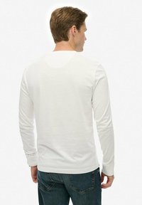 Langarmhemd aus weichem Stoff in Weiß mit Rundhalsausschnitt und gerippten Manschetten, kombiniert mit blauen Jeans, von hinten sichtbar.