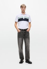 Valkoinen polo-paita, jossa on tummansinisiä ja mintunvihreitä vaakaraitoja, yhdistettynä haalistuneisiin harmaisiin farkkuihin ja mustiin kenkiin. Rentomallinen, lyhyet hihat, klassinen kaulus.