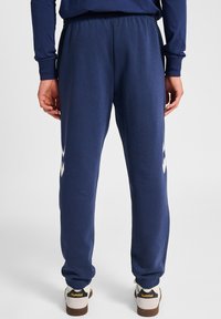 Granatowe spodnie dresowe z elastycznym paskiem i mankietami, z białym detalem logo z boku, wykonane z miękkiego, oddychającego materiału.