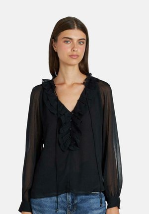 Blusa de gasa negra con mangas largas, cuello en V, detalles con volantes y botones en la parte delantera. Tejido ligero y transparente con lazos ajustables en el cuello.