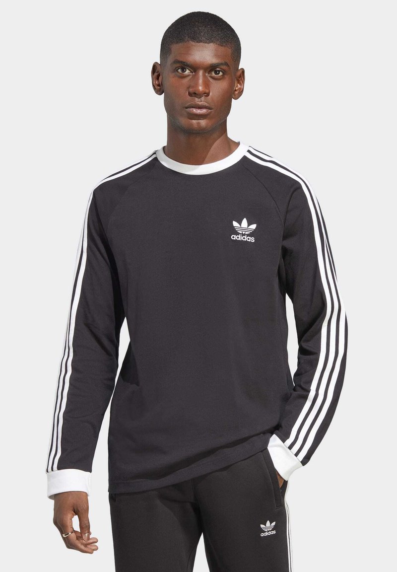 Čierna dlhá rukávová košeľa s bielym golierom a tromi bielymi pruhmi na rukávoch. Na hrudi sa nachádza malé biele logo Adidas.