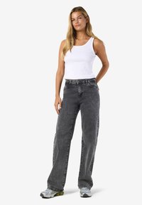 Ribbade vita linne ihop med hög midja, löst sittande grå denimjeans. Modellen bär grå och gröna sneakers. Enkel, avslappnad look.