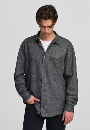 Camicia di flanella grigia scura con maniche lunghe, chiusura con bottoni sul davanti, taschino singolo sul petto e una consistenza morbida. Sottile motivo tessuto.