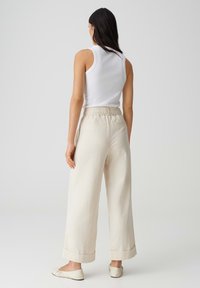 Ontspannen pasvorm, hoog-taille beige broeken met een brede pijp, elastische tailleband en opgerolde manchetten, gecombineerd met een strak fitting witte tanktop en platte schoenen.