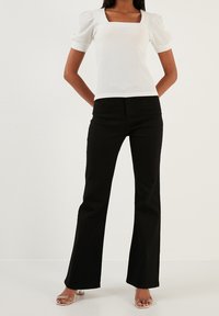 Biały top z kwadratowym dekoltem i bufiastymi krótkimi rękawami, połączony z czarnymi spodniami dzwonowymi. Strój charakteryzuje się gładką fakturą i dopasowanym krojem.