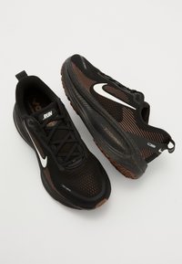 Black athletic shoes with orange accents, textured mesh upper, rubber outsole, and white logo. Features lace-up design and pull tab.