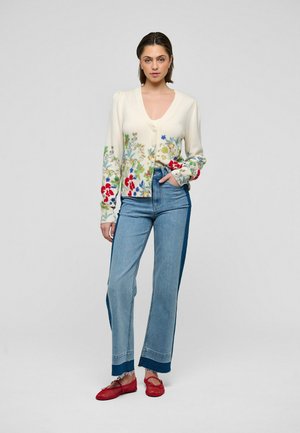Cardigan lavorato a maglia con ricamo floreale in crema, abbinato a jeans denim a vita alta e ballerine rosse, caratterizzati da gambe larghe e design bicolore.
