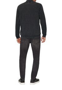 Zwarte denimjack met een kraag, lange mouwen, geribde manchetten en boord. Gecombineerd met donker grijze jeans en zwarte sneakers met witte zolen.