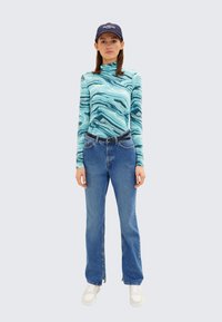 En ljusblå långärmad topp med ett marmorliknande mönster, tillsammans med högmidjade blå jeans och vita sneakers. Modellen har på sig en marinblå keps.