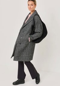 Gray herringbone coat with oversized fit, double-breasted front, large lapels, paired with black bag and black high-top sneakers.
