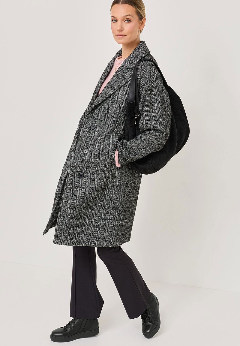 Gray herringbone coat with oversized fit, double-breasted front, large lapels, paired with black bag and black high-top sneakers.