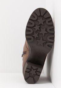 Semelle de botte marron avec motifs de crampons en forme d'étoile et taille 37 imprimée en bas, positionnée en angle sur un fond d'angle blanc.