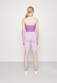 Top corto morado con cuello halter y textura brillante, combinado con pantalones cortos de ciclista morados claros hasta la rodilla. Zapatillas blancas completan el atuendo.