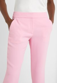 Rosa byxor i ett slätt tyg med rak bendesign och sidofickor. Har en flat midja och rena sömmar.