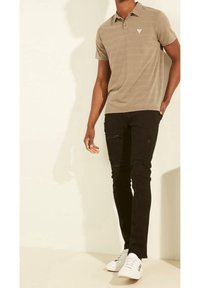 Polo beige à manches courtes avec un petit emblème, associé à un jean noir déchiré et des baskets blanches. Design simple et ajusté.