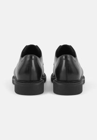Chaussures en cuir noir avec une texture lisse, bout rond et semelles en caoutchouc. Design minimaliste avec des détails de couture subtils.