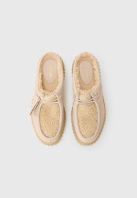 Beige slip-on shoes with a soft, fluffy shearling lining, leather-like exterior, and rubber soles featuring a serrated edge for traction.