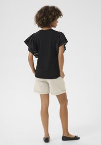 Černý top s volánkovými rukávy, v kombinaci s béžovými šortkami. Tento outfit má uvolněný střih a jemnou texturu látky.