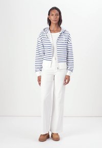 Haut à capuche zippé bleu et blanc à rayures, avec des poignets et un ourlet côtelés, associé à un pantalon large blanc et des chaussures plateformes brunes.