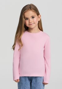 Różowa bawełniana koszulka z długim rękawem, okrągłym dekoltem, gładką fakturą i luźnym krojem, noszona z niebieskimi dżinsami.