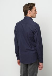 Camisa de botones azul marino con textura lisa, de mangas largas y cuello estándar. Presenta un dobladillo curved y botones negros.