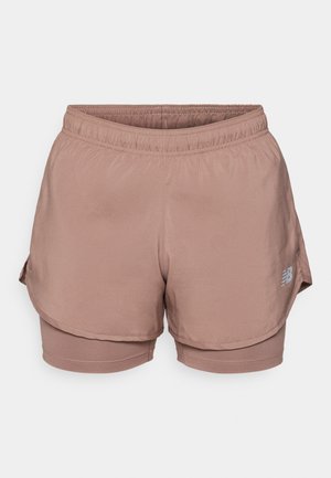 Light pink athletic shorts feature an elastic waistband, layered design, and a reflective logo detail on the side. Smooth fabric.
