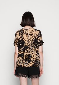 T-shirt à manches courtes beige avec imprimé léopard noir, présentant un col rond et un petit détail en découpe dans le dos.