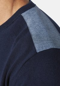 Marineblaues Strickpullover mit einer strukturierten hellblauen Applikation an der Schulter, runder Ausschnitt und gerippten Bündchen.