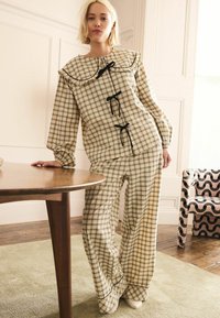 Karirana bombažna loungewear postava v bež in črni barvi, z nabranim ovratnikom, dolgimi rokavi in naglavnimi naglasi na vrhu in hlačah.