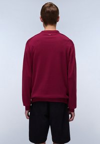 Suéter de manga larga burdeos con cuello redondo, puños y dobladillo acanalados. Textura suave. Llevado con pantalones cortos negros. Sin marcas visibles.