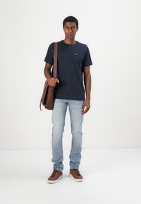 Navy cotton t-shirt with a small logo, light blue denim jeans, brown leather sneakers, and a brown leather shoulder bag.