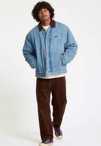 Blå denimjakke med brun fløjlskrave, forreste trykknaplukning og sidelommer, kombineret med brune fløjlsbukser og lilla sneakers.