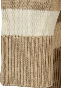 Manche de pull en tricot beige avec des rayures horizontales crème ; la texture côtelée du poignet rehausse l'intérêt visuel et le détail.