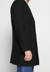 Černé kostkované sako s přizpůsobeným střihem, s klopovým límcem s výbrusem, bočními kapsami a detaily tříknoflíkových manžet. Texturovaná látka.