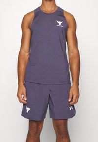 Man som bär en matchande mörkgrå ärmlös träningströja och shorts med vita tjurkranium-logotyper och texten "Project Rock" ovanpå.