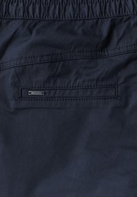 Granatowe, lekkie szorty wykonane z tkaniny, z elastycznym pasem, posiadające jedną tylną kieszeń z małą metką z logo oraz minimalne detale szwów.