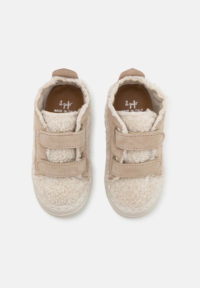 Sneakers beige per bambini con una morbida e soffice texture, dotati di due strap in Velcro e suola in gomma bianca, progettati per comfort e facilità di utilizzo.
