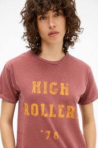 Maroon t-shirt made of soft fabric, featuring a worn yellow print saying "HIGH ROLLER. '78" across the chest. Short sleeves and crew neck.