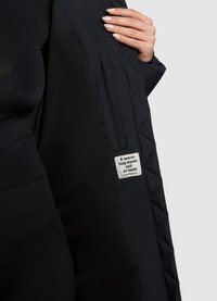 Chaqueta negra acolchada con un forro interior suave, que presenta una etiqueta de tela que dice "Un abrazo cálido hecho de tela."