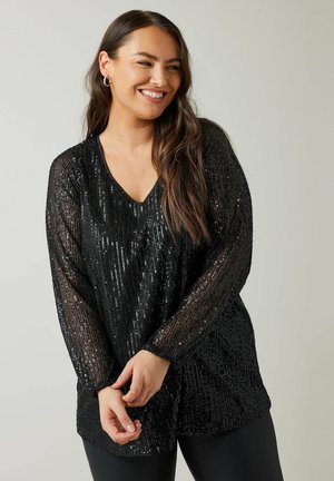 Zwarte pailletten top met een V-hals en lange mouwen, met een losse pasvorm en een glanzende textuur, gecombineerd met zwarte leggings.