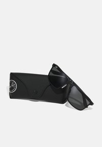 Ochelari de soare negri cu un design elegant și unghiular și lentile întunecate, așezați lângă un toc texturat negru cu un logo circular.