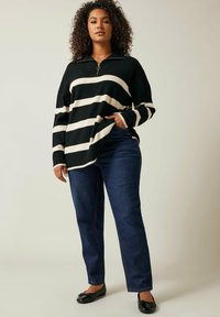 Mustassa ja beigen raidallisessa neulepaidassa on vetskari kauluksessa, yhdistetty tummansiniset suorat farkut ja mustat ballerinat. Rento tyyli, pitkät hihat.