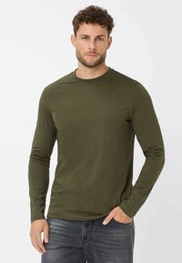 Langärmliges T-Shirt in Olivgrün mit Rundhalsausschnitt und glattem Baumwollgewebe. Modell trägt es zu dunklen Jeans.