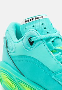 Detailní záběr na tyrkysovou tenisku s patterned podešví, pleteným jazykem s nápisem "NB FF BB v2" a odpovídajícími tkaničkami.