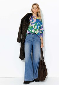 Un pull coloré à motifs de feuilles, un jean bleu à jambes larges, un manteau à imprimé léopard brun et un sac fourre-tout en suède brun, le tout sur un fond blanc.