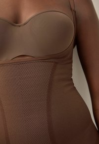 Smeđi bodysuit bez naramenica, s glatkim materijalom i teksturiranim chevron uzorkom na tijelu za prilagođen izgled.
