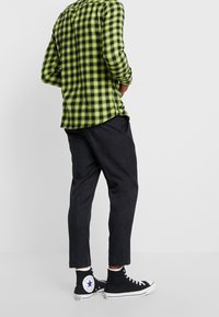 Groene en zwarte geruite flanellen overhemd met lange mouwen, gecombineerd met donkere, taps toelopende broeken en zwarte hoge sneakers.