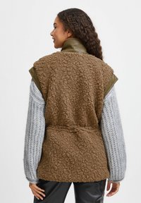 Vesta din imitație de blană maro cu accente din piele ecologică verde, design supradimensionat, spate deschis și mâneci tricotate gri.