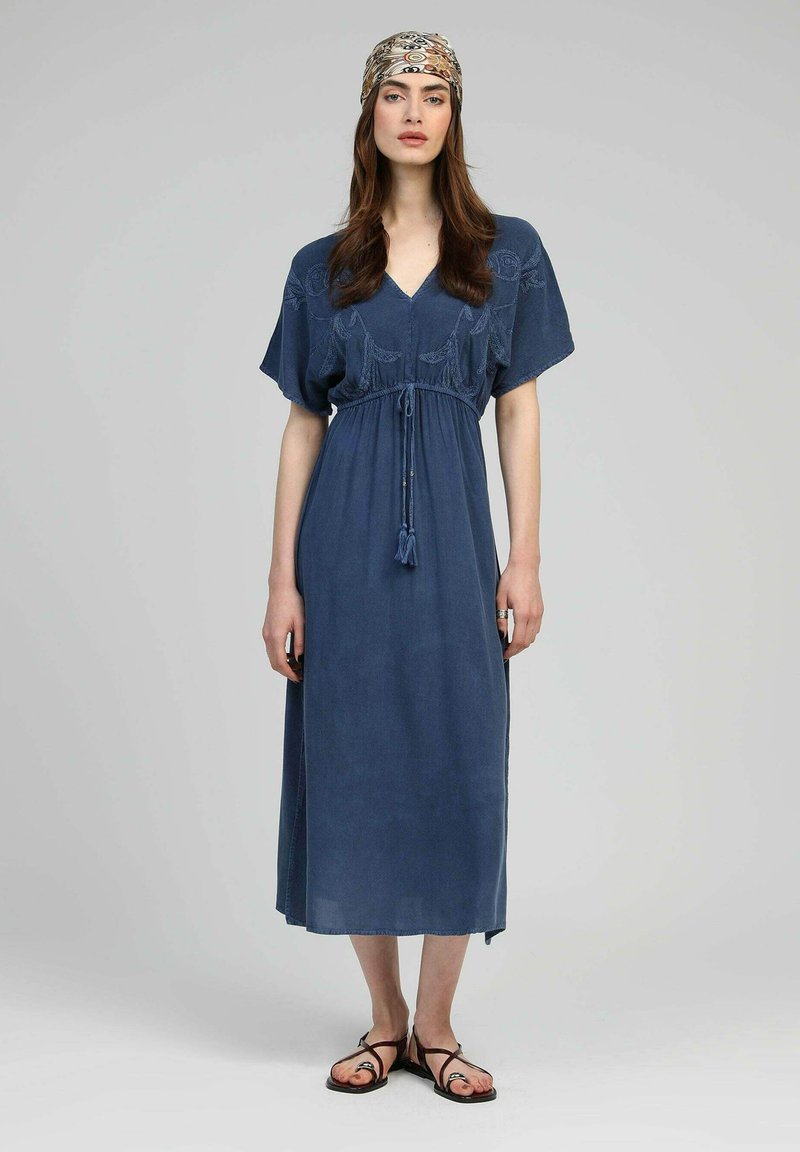 Robe maxi en coton bleu avec des manches courtes, taille à cordon, détails en à pompons et broderie florale sur le buste.